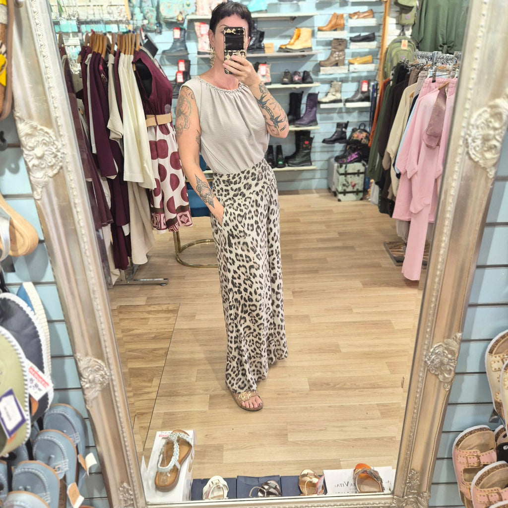 A woman wearing runway boutique high-waisted wide-leg leopard print trousers and a beige top in a clothing store.